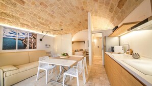A cozy interior with a stone ceiling, a dining area with a table and chairs, a sofa, and a kitchen area with a sink and countertop. - TD Casa Kairos Cozy Smart Apartment in the Center (Polignano a Mare)