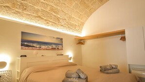A bedroom with a large bed, a painting of a beach, and a wooden shelf. - TD Casa Kairos Cozy Smart Apartment in the Center (Polignano a Mare)