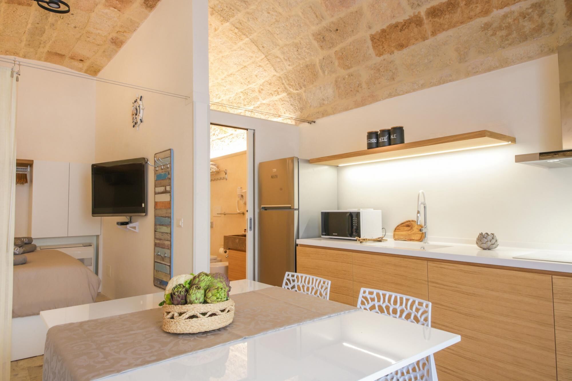 A modern kitchen with a white countertop, wooden cabinets, a built-in microwave, and a basket of fresh produce on the table.