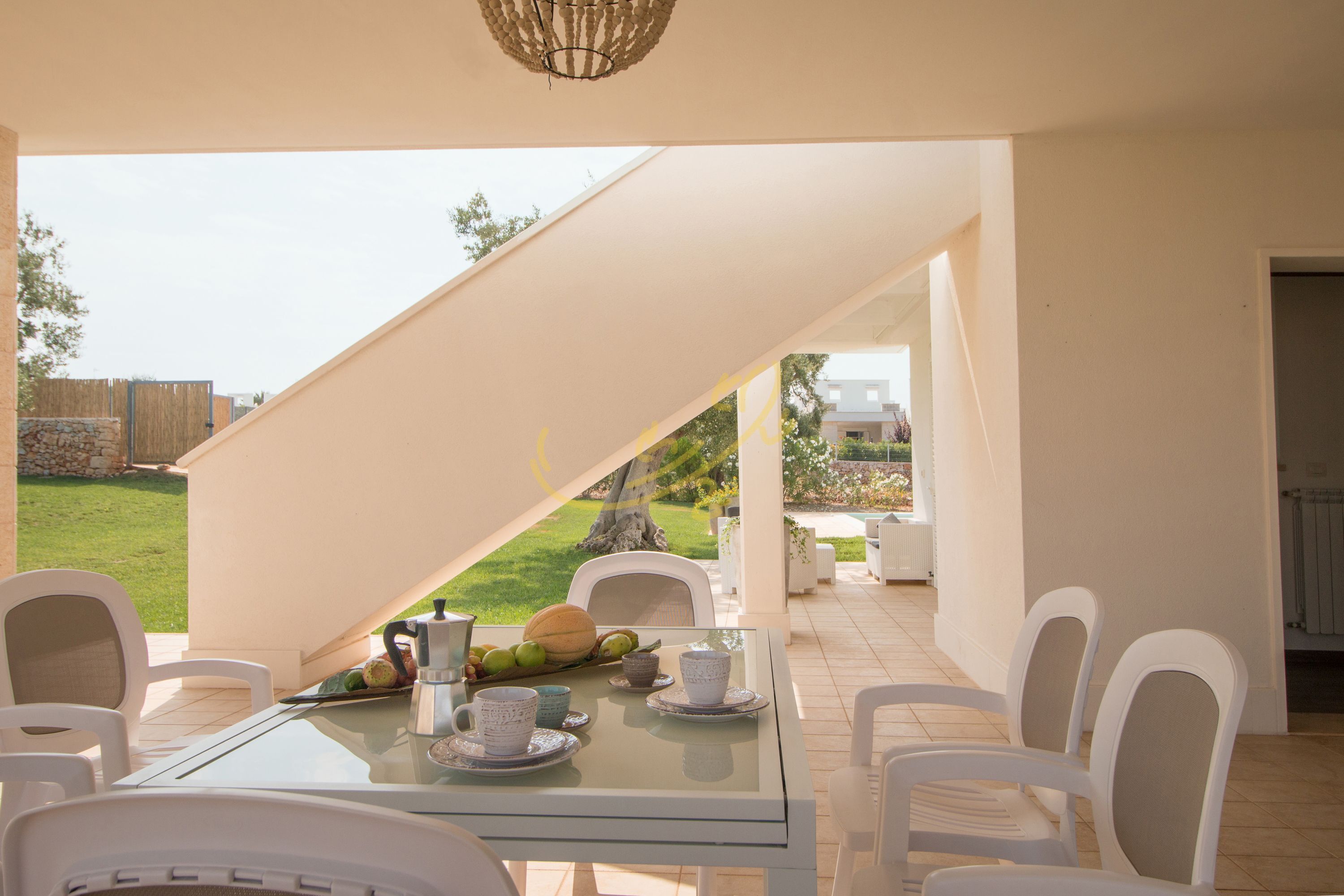 A dining area with a glass table, white chairs, and a view of the garden.