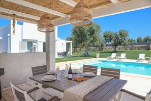 An outdoor dining area with a pool view, wicker hanging lights, and a table set for a meal. - TD Villa Patrizia Pool Alfresco Kitchen (Monopoli)