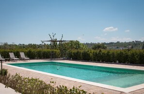 Piscina retangular com pérgola e espreguiçadeiras, rodeada por sebes e vista para uma paisagem montanhosa.