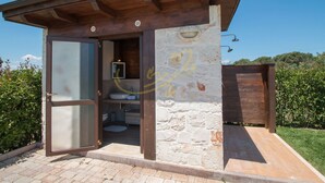 A rustic outdoor bathroom with a stone wall, wooden beams, and a glass door.