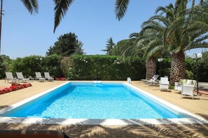 Una piscina rettangolare con acqua cristallina e azzurra, circondata da sdraio bianche e palme.