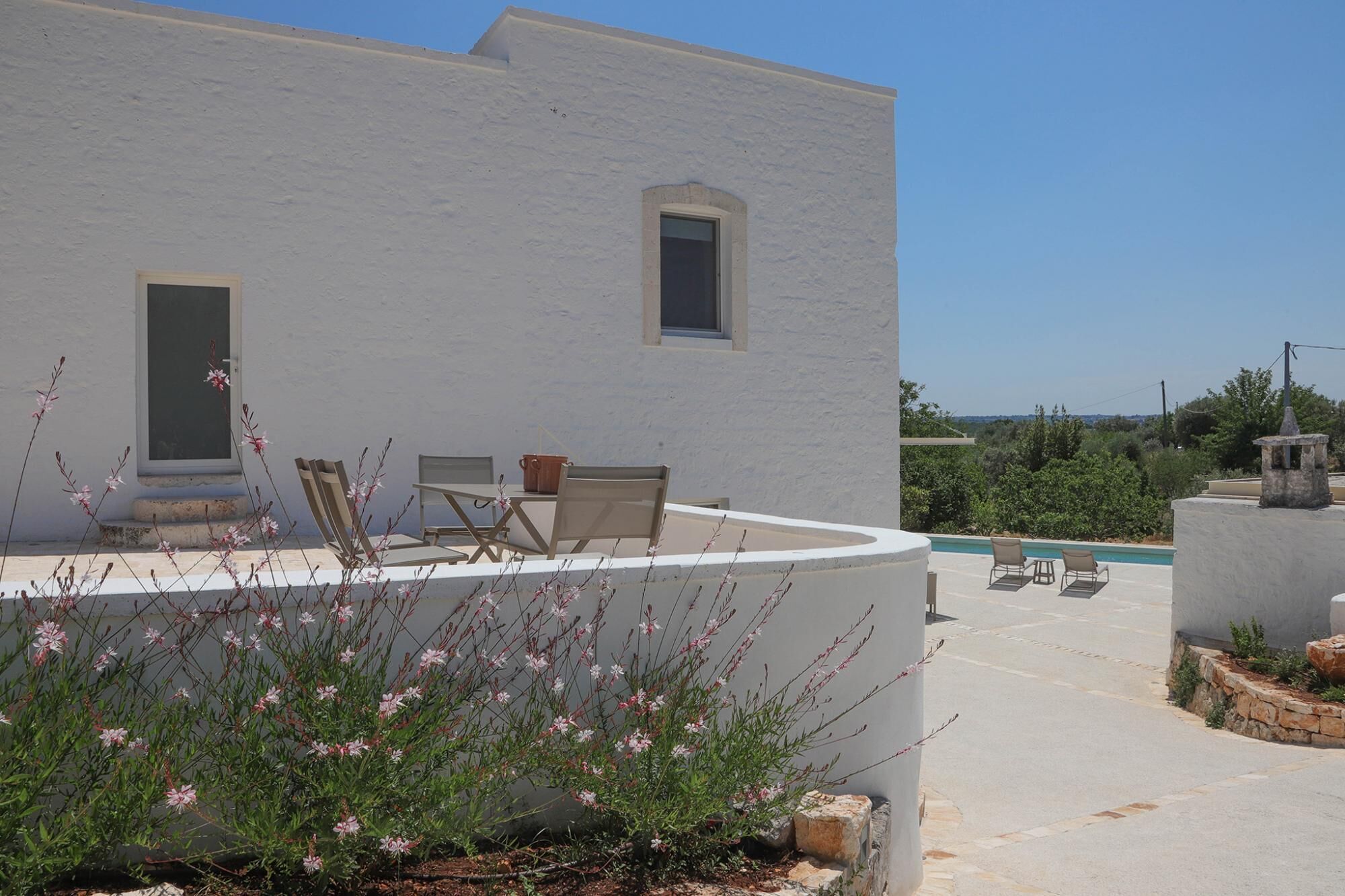 Un edificio bianco con piscina, area salotto esterna e piante fiorite.