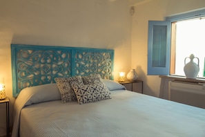 A bedroom with a bed, decorative headboard, bedside lamps, and a window with a view. - TD Casa Reina in the Historic Center With Terrace (Polignano a Mare)