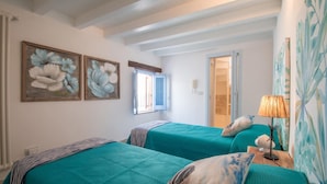 A room with two beds, each with teal bedding and pillows, a wooden headboard, a window with a blue door, and a wall with floral paintings. - TD Casa Reina in the Historic Center With Terrace (Polignano a Mare)