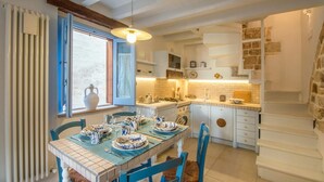 A dining area with a table set for four, a window with curtains, and a kitchen area with a stove and cabinets. - TD Casa Reina in the Historic Center With Terrace (Polignano a Mare)