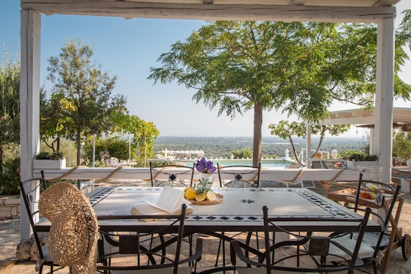 Enjoy al fresco dining with a view of the surrounding landscape from this outdoor dining area, complete with a beautifully set table and a charming pergola.