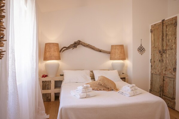 A neatly made bed with white linens and towels, two bedside lamps, a rustic wooden headboard, and a wooden wardrobe. - TD Villa Fico Jo Villa With Pool Lush Garden (Polignano a Mare)