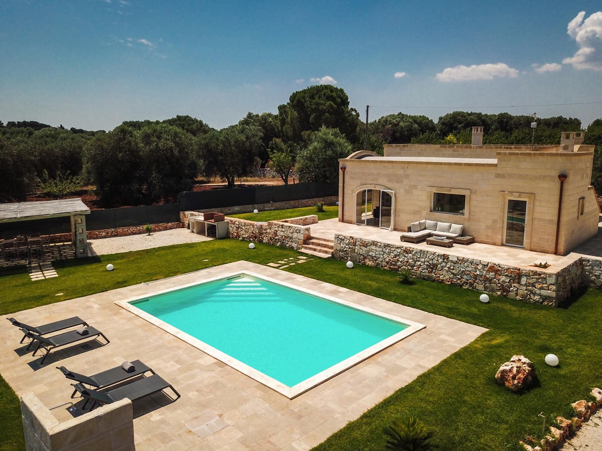A modern house with a swimming pool, outdoor seating, and a stone wall.