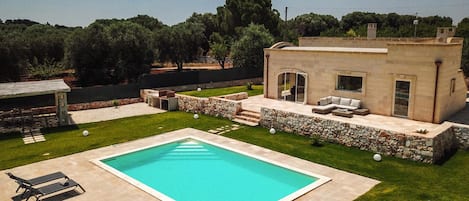 A modern house with a swimming pool, outdoor seating, and a stone wall.