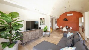 Una sala de estar con televisor, un comedor con mesa y sillas, y una cocina con armarios.