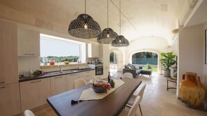 Una cocina amplia con una isla grande, lámparas colgantes modernas y vistas al exterior a través de un ventanal.