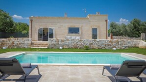 Una villa de piedra con piscina, mobiliario exterior y un muro de piedra.