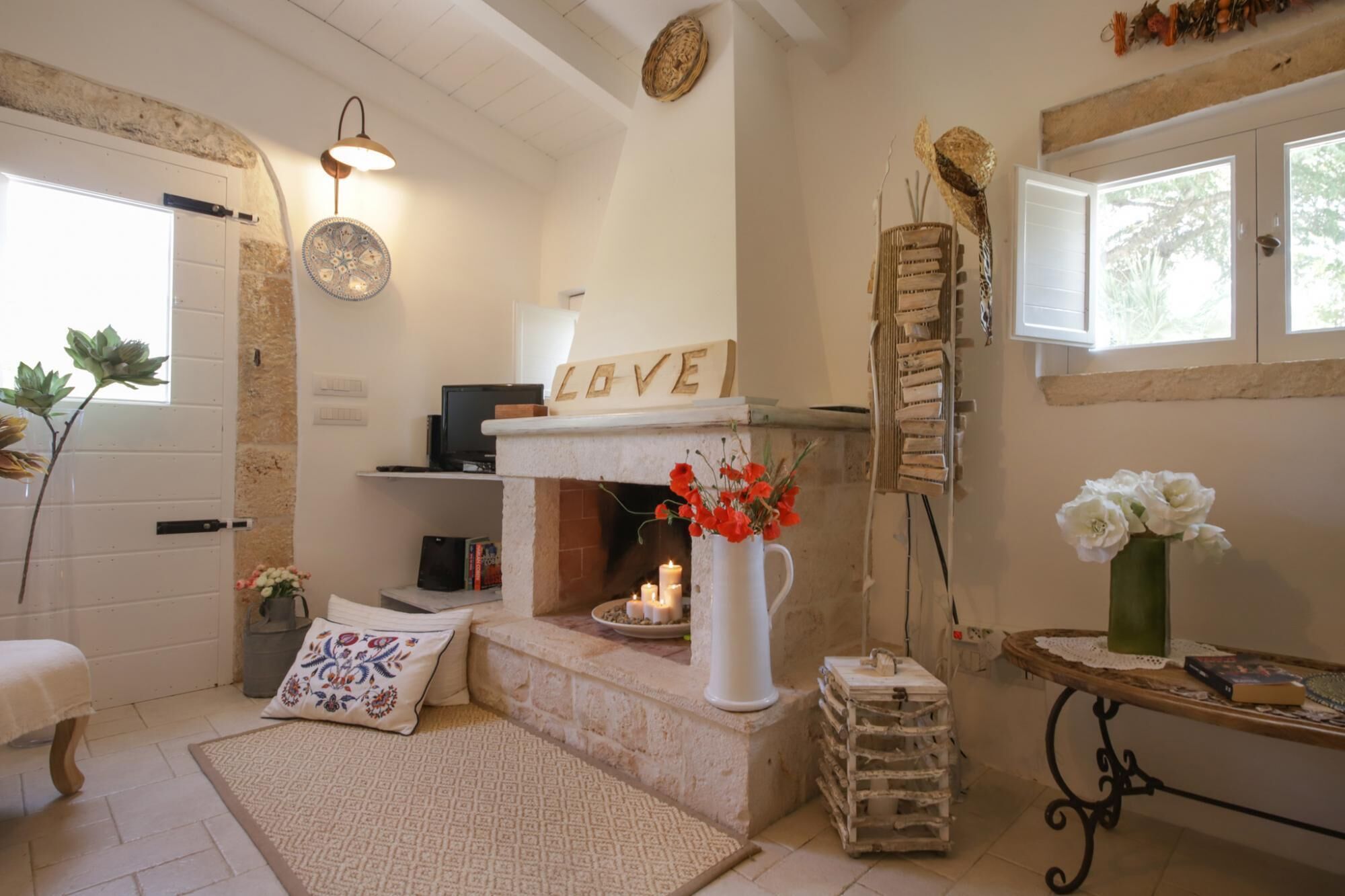 A cozy room with a fireplace, a desk with a computer, and a window with a view of greenery.