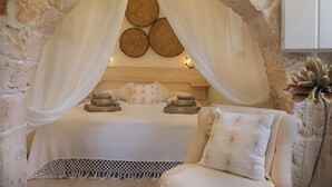 Ein Schlafzimmer mit steinernen Rundbogen, einem Bett mit weißen Leinen, einem Baldachin und einem Nachttisch mit Handtüchern.