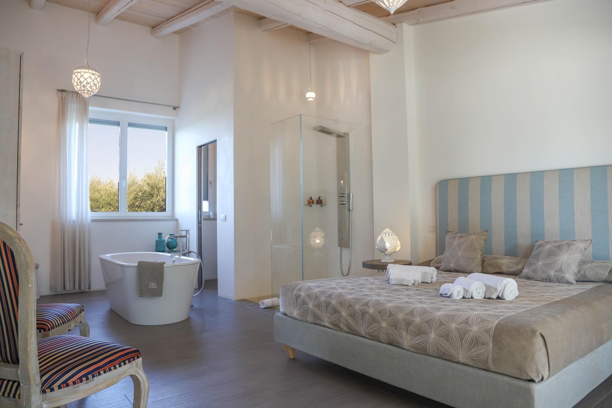 Un dormitorio con una cama grande, una zona de estar con una silla, una bañera y una ducha.