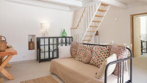 Un salon chaleureux avec un canapé, une table basse en bois, un meuble noir aux portes vitrées, un vase vert et un escalier.