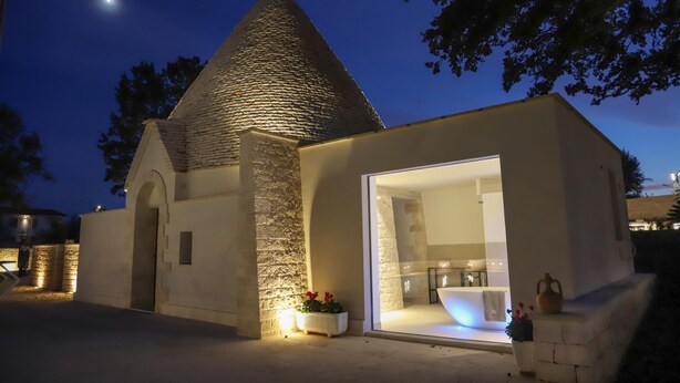 Un bâtiment moderne avec un toit conique en pierre, une grande entrée vitrée et un petit espace extérieur aménagé avec des fleurs.