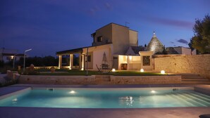 A modern house with a swimming pool, a covered patio, and a stone wall. - TD Trulli Saveni Trulli With Pool Near the Centre (Castellana Grotte)