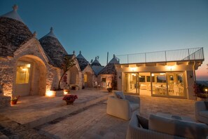 Um edifício de pedra com vários telhados cônicos, um pátio coberto com área de estar externa e uma área envidraçada com iluminação interna.