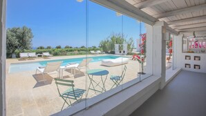 Ein Poolbereich mit Liegestühlen und einem Tisch, eine Pergola mit Blick und eine Terrasse mit Topfpflanzen.