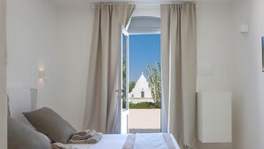 Ein Schlafzimmer mit Bett, Kissen und Blick auf ein weißes Gebäude durch einen Durchgang.