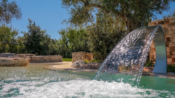 A water feature with a cascading waterfall in a landscaped area with rocks and trees. - TD Trulli di Montaltino With Stunning Huge Pool (Polignano a Mare)