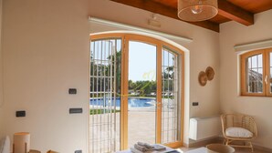 A room with a bed, a chair, a table, and a view of a swimming pool through a glass door. - TD Trulli Bruco Large Pool for Family Fun (Monopoli)