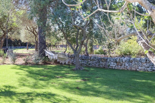A stone wall and a hammock in a grassy area with trees. - TD Trulli Tortorella w Nature Pool Sauna (Monopoli)