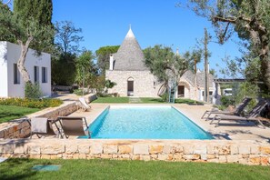 A swimming pool with stone walls, lounge chairs, and a stone building with a conical roof in the background. - TD Trulli Tortorella w Nature Pool Sauna (Monopoli)