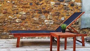 Un banc en bois avec une assise et un dossier noirs, une petite table et une plante en pot.
