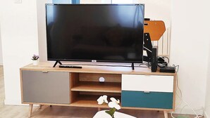 Un salon moderne avec un téléviseur à écran plat, un meuble de rangement en bois, une table basse blanche et un pot d’orchidée.