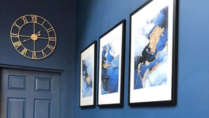 A hallway with a blue door, a wall-mounted clock, and three framed abstract paintings. - Junior suite within walking distance of York city centre (York)