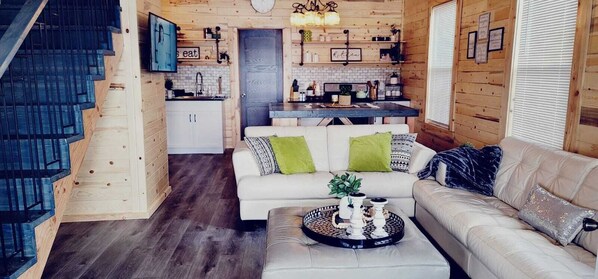 A cozy cabin interior with a staircase, a dining area, and a living room with a sofa and coffee table. - Lakefront Heritage Cabin on Lake Victoria – Steps from the Water! (Alexandria)