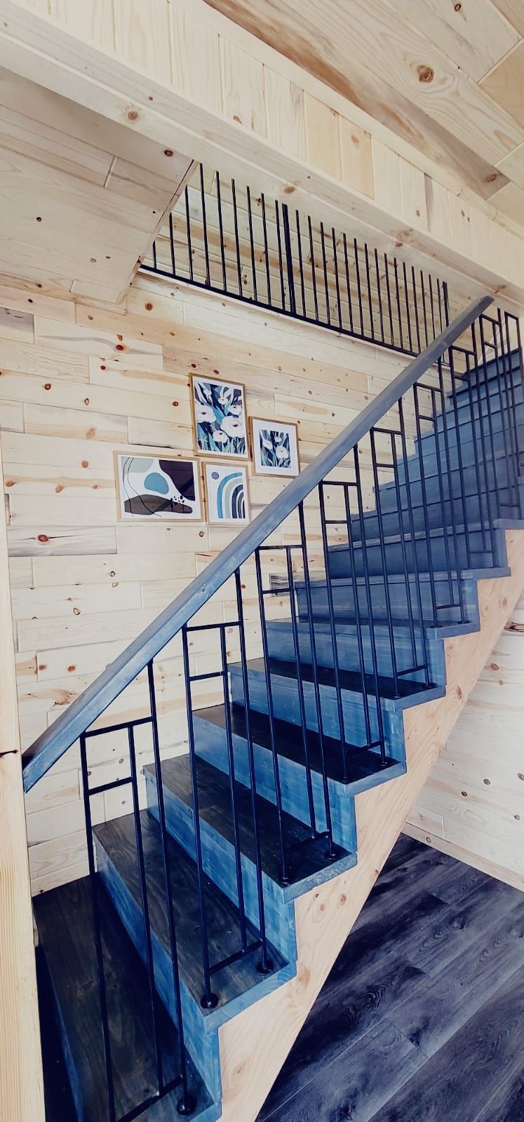 A wooden staircase with black railings and a handrail, leading to an upper level.