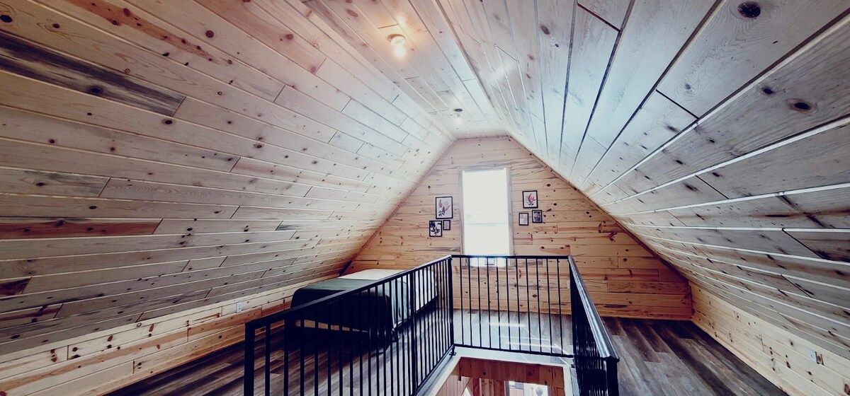A sloped ceiling with wooden paneling, a black metal railing, and a small window.