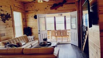 A log cabin interior with a sofa, dining table, chairs, and a view through a door.