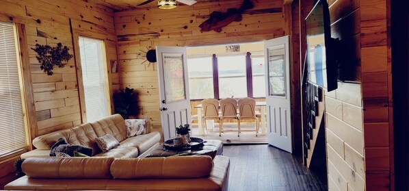 A log cabin interior with a sofa, dining table, chairs, and a view through a door.