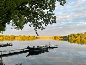 A calm lake with a dock and a boat named "ALUMACRAFT". - Lakefront Heritage Cabin on Lake Victoria – Steps from the Water! (Alexandria)