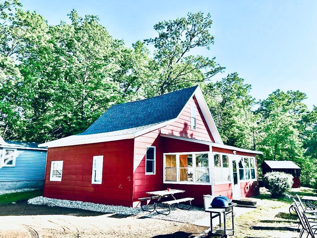Une maison en bois rouge, avec un toit à pignon, un porche et une petite table avec une chaise placée à l’extérieur.