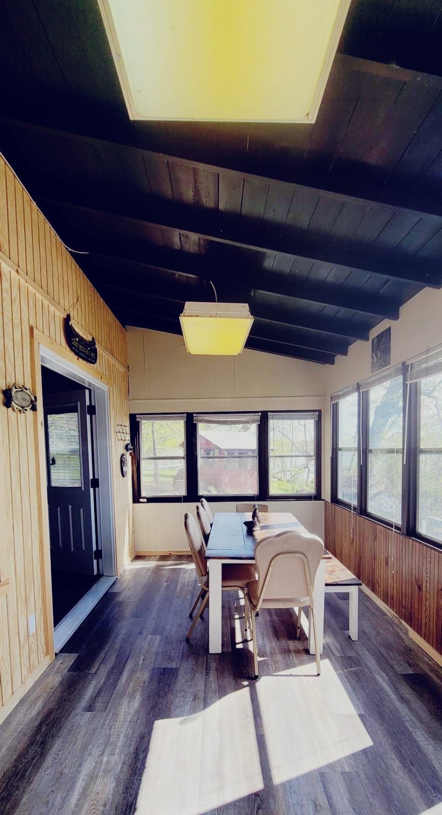 A room with a wooden interior, a table with chairs, a ceiling light, and windows.