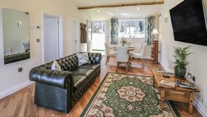 Un salon spacieux avec un canapé en cuir, un coin repas comprenant une table et des chaises, un grand miroir et un téléviseur fixé au mur.