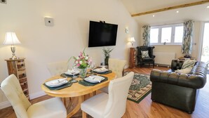 Un coin repas avec une table en bois, dressée pour quatre personnes, entourée de chaises blanches. Un téléviseur à écran plat est fixé au mur, au-dessus de la table.
