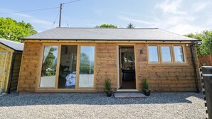 Une cabane en bois dotée de grandes fenêtres, une allée en gravier et une clôture en bois en arrière-plan.