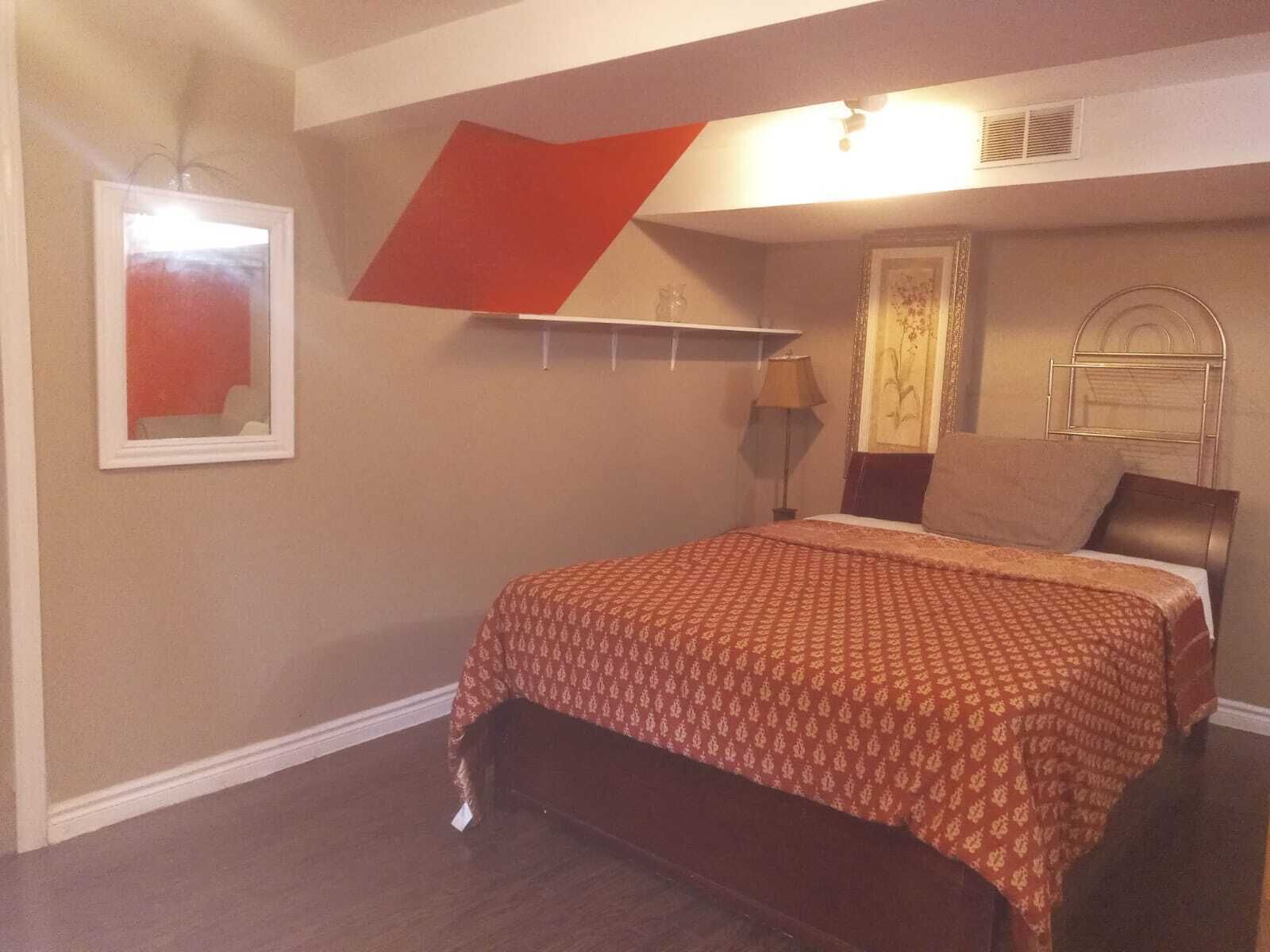 A bedroom with a bed, a nightstand, a lamp, a mirror, and a red accent wall.