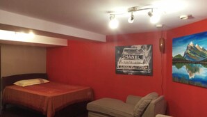 A room with a bed, a sofa, a red wall, and a painting of a mountain landscape. - COZY APARTMENT FOR RENT GREEN NEIGHBORHOOD (Mississauga)