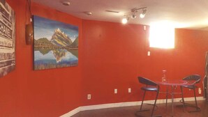 A room with red walls, a painting of a mountain landscape, a table with chairs, and a guitar leaning against the wall. - COZY APARTMENT FOR RENT GREEN NEIGHBORHOOD (Mississauga)