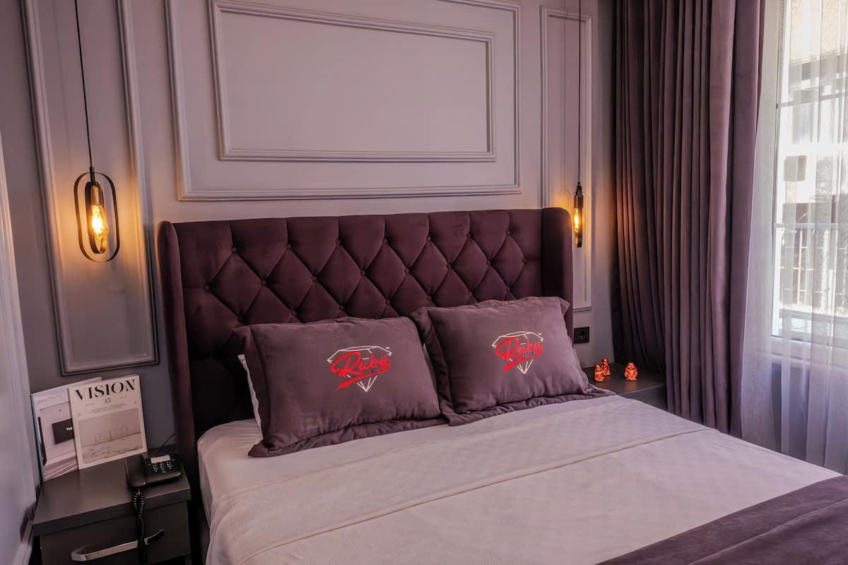 A neatly made bed with a tufted headboard, two pillows with a logo, a bedside table with a lamp, and a sign on the wall.